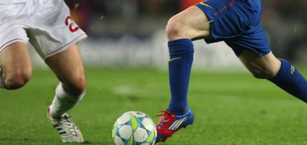 Two footballers from opposing teams about to kick a ball